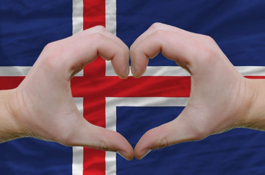 Gesture made by hands showing symbol of heart and love over iceland flag