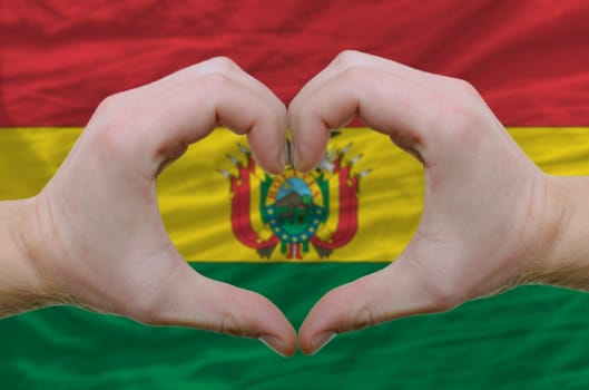 Gesture made by hands showing symbol of heart and love over bolivia flag