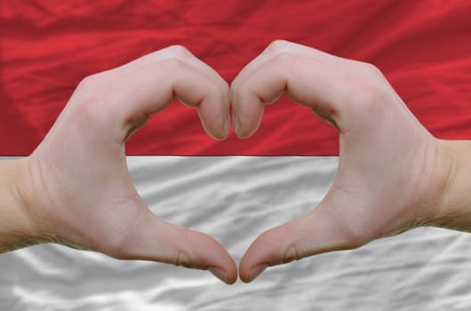 Gesture made by hands showing symbol of heart and love over indonesia flag