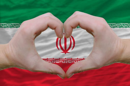 Gesture made by hands showing symbol of heart and love over iran flag