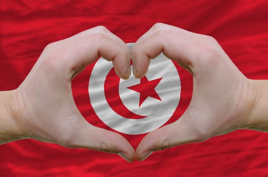 Gesture made by hands showing symbol of heart and love over tunisia flag