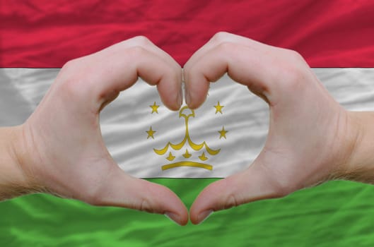 Gesture made by hands showing symbol of heart and love over tajikistan flag