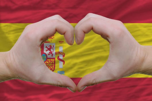 Gesture made by hands showing symbol of heart and love over spain flag