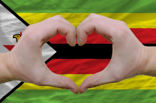 Gesture made by hands showing symbol of heart and love over zimbabwe flag