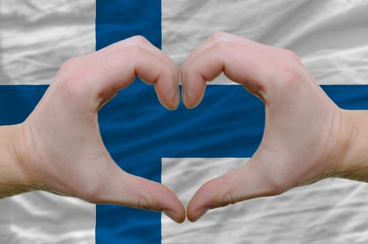 Gesture made by hands showing symbol of heart and love over finland flag