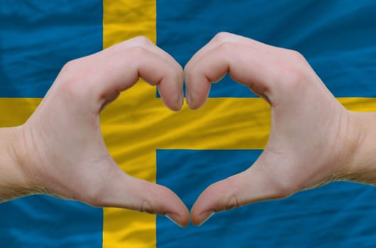 Gesture made by hands showing symbol of heart and love over sweden flag