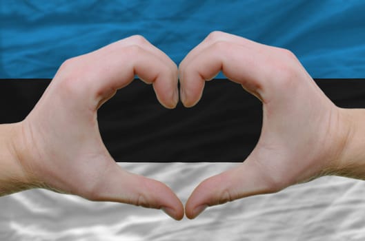 Gesture made by hands showing symbol of heart and love over estonia flag