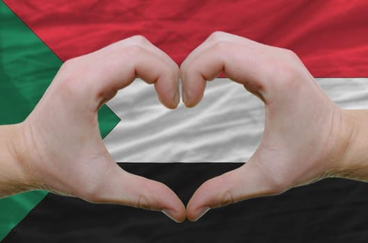 Gesture made by hands showing symbol of heart and love over sudan flag