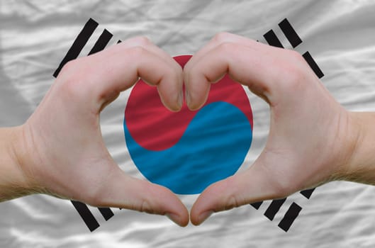 Gesture made by hands showing symbol of heart and love over south korean flag