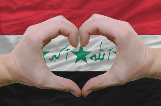 Gesture made by hands showing symbol of heart and love over iraq flag