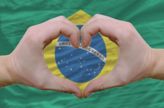 Gesture made by hands showing symbol of heart and love over brazilian flag