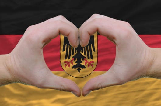 Gesture made by hands showing symbol of heart and love over germany flag