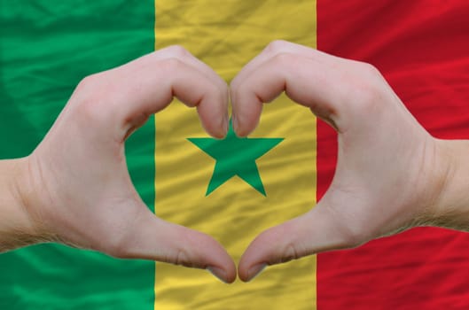 Gesture made by hands showing symbol of heart and love over senegal flag