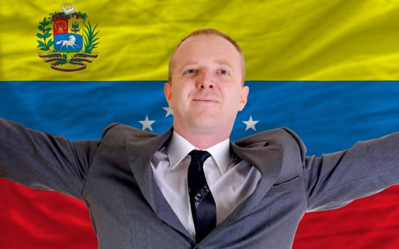 joyful investor spreading arms after good business investment in venezuela, in front of flag