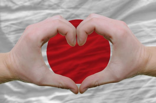 Gesture made by hands showing symbol of heart and love over japan flag