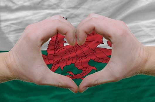 Gesture made by hands showing symbol of heart and love over wales flag