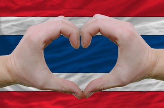 Gesture made by hands showing symbol of heart and love over thailand flag