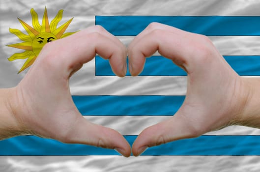 Gesture made by hands showing symbol of heart and love over uruguay flag