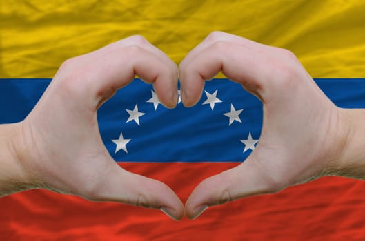 Gesture made by hands showing symbol of heart and love over venezuela flag