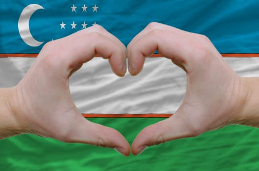 Gesture made by hands showing symbol of heart and love over uzbekistan flag
