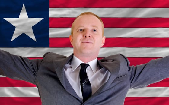 joyful investor spreading arms after good business investment in liberia, in front of flag