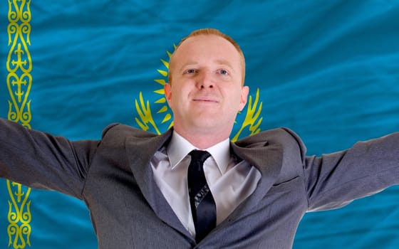 joyful investor spreading arms after good business investment in kazakhstan, in front of flag