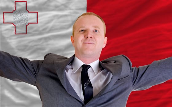 joyful investor spreading arms after good business investment in malta, in front of flag