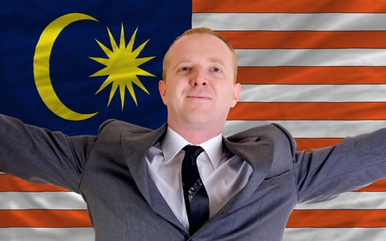 joyful investor spreading arms after good business investment in malaysia, in front of flag