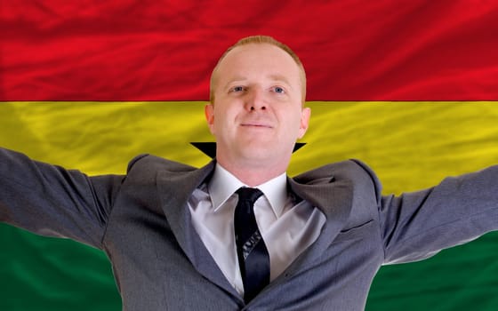 joyful investor spreading arms after good business investment in ghana, in front of flag