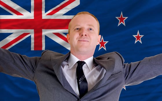 joyful investor spreading arms after good business investment in new zealand, in front of flag