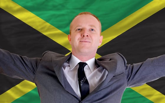 joyful investor spreading arms after good business investment in jamaica, in front of flag