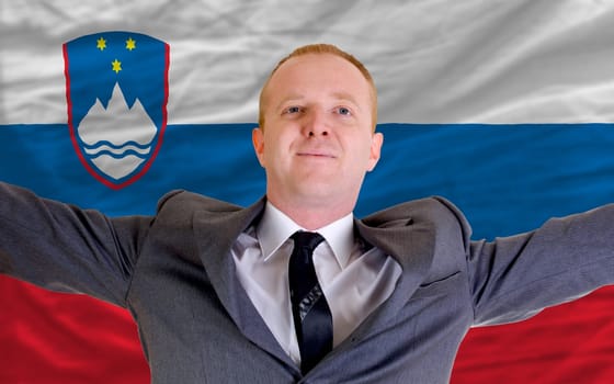 joyful investor spreading arms after good business investment in slovenia, in front of flag