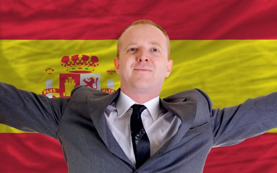 joyful investor spreading arms after good business investment in spain, in front of flag