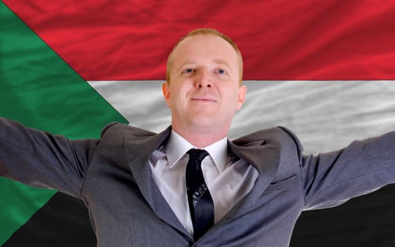 joyful investor spreading arms after good business investment in sudan, in front of flag