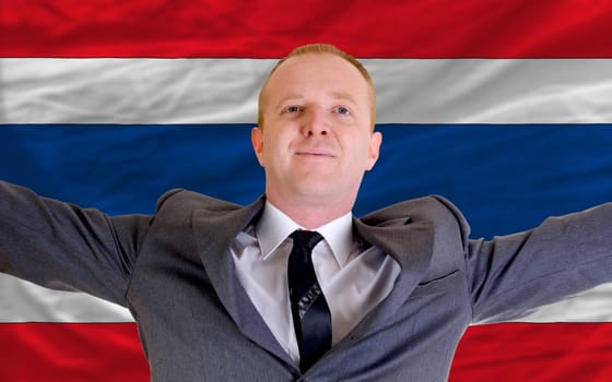 joyful investor spreading arms after good business investment in thailand, in front of flag