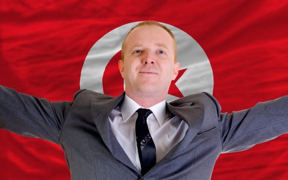 joyful investor spreading arms after good business investment in tunisia, in front of flag