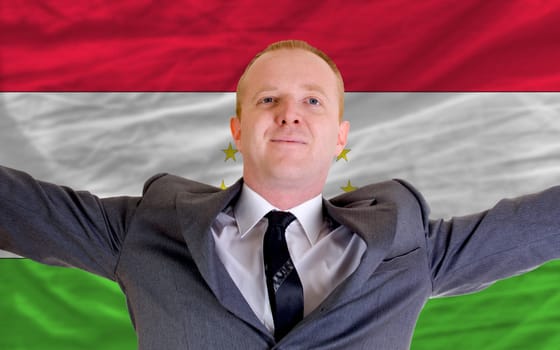 joyful investor spreading arms after good business investment in tajikistan, in front of flag