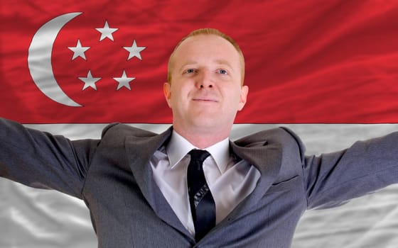 joyful investor spreading arms after good business investment in singapore, in front of flag
