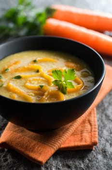 Fresh carrot soup in black bowl close up