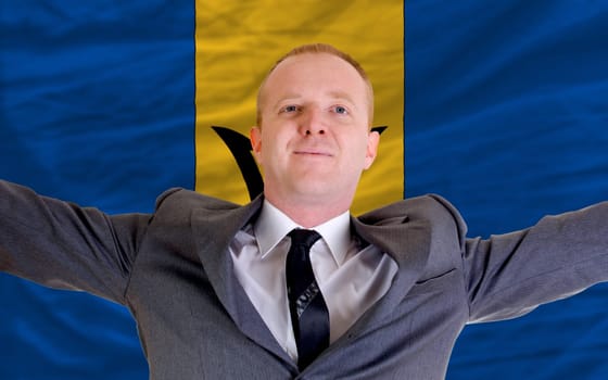joyful investor spreading arms after good business investment in barbados, in front of flag