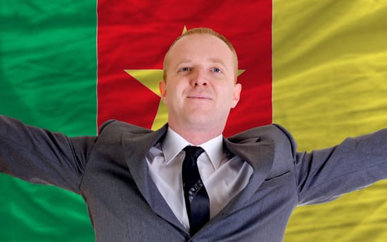 joyful investor spreading arms after good business investment in cameroon, in front of flag