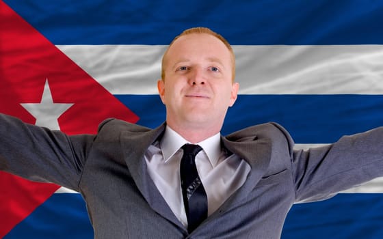 joyful investor spreading arms after good business investment in cuba, in front of flag