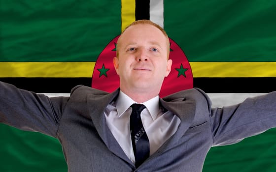 joyful investor spreading arms after good business investment in dominica, in front of flag