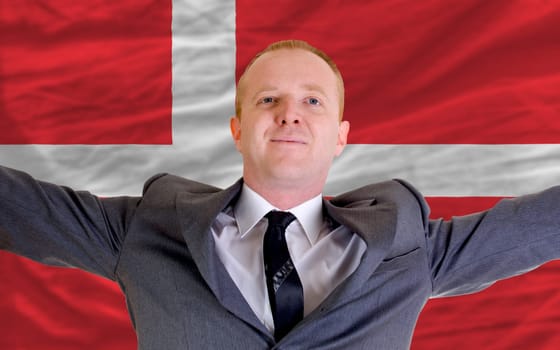joyful investor spreading arms after good business investment in denmark, in front of flag