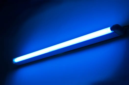 One fluorescent lamp shining on blue colored wall