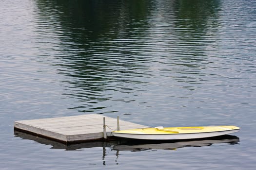 A small yellow boat tied to a dock on a lake.