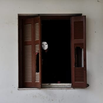 Man with white mask by the broken window shutter of an abandoned house.