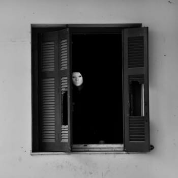 Masked figure by the broken windows of an abandoned house.