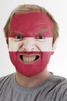 High key portrait of an angry man whose face is painted in colors of latvia flag