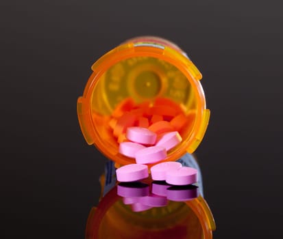 Set of round purple tablets pouring from an orange pill bottle